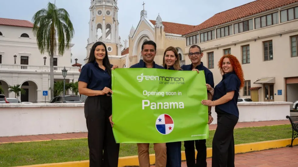 Five Panama-based Green Motion employees holding a green banner sign in front of historical building in Panama City, Panama.