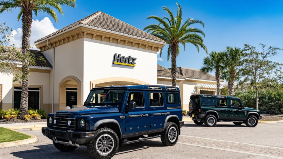 Photos of two black INEOS Grenadier 4x4 vehicles in front of a Hertz rental car outlet.