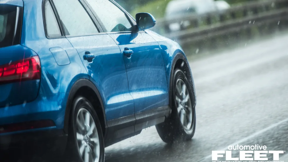 A blue SUV drives on wet pavement as rain comes down.