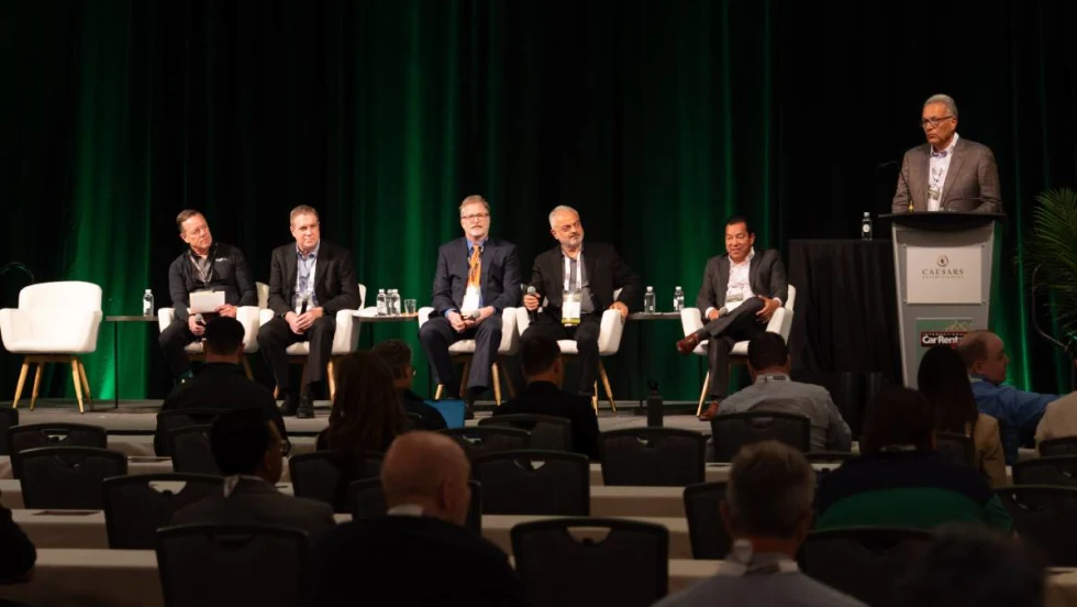 Five panelists sitting in white chairs and a moderator at the podium on stage at ICRS