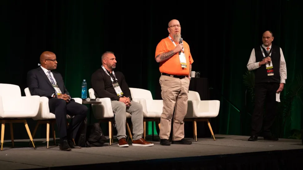 Panelists seated and standing on stage at conference.