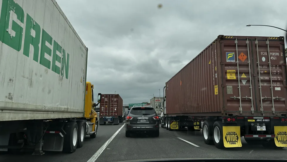 A passenger car stuck in traffic on highway next to big rigs.