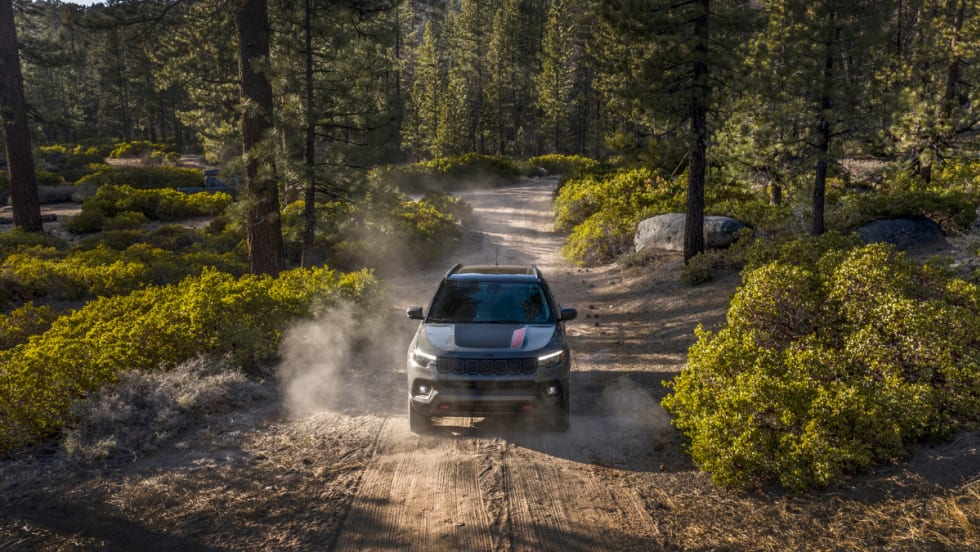 A photo of the 2026 Jeep Compass driving on a dirt road through the woods.