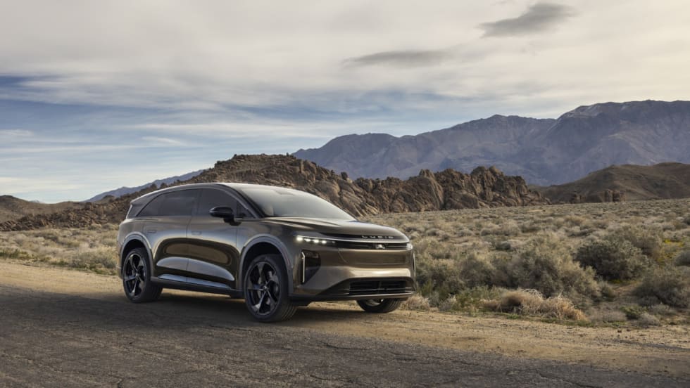 Lucid Gravity electric SUV parked on a desert road with mountains in the background, showcasing updated 2027 model with revised trims and added standard features.