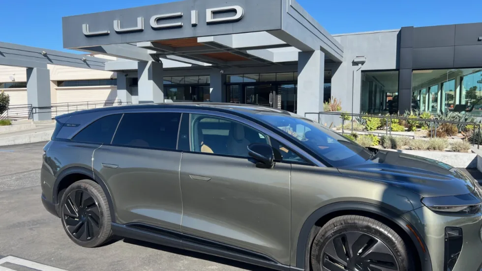 A right-side view of a gray Lucid Gravity Grand Touring in front of a Lucid dealership entrance.
