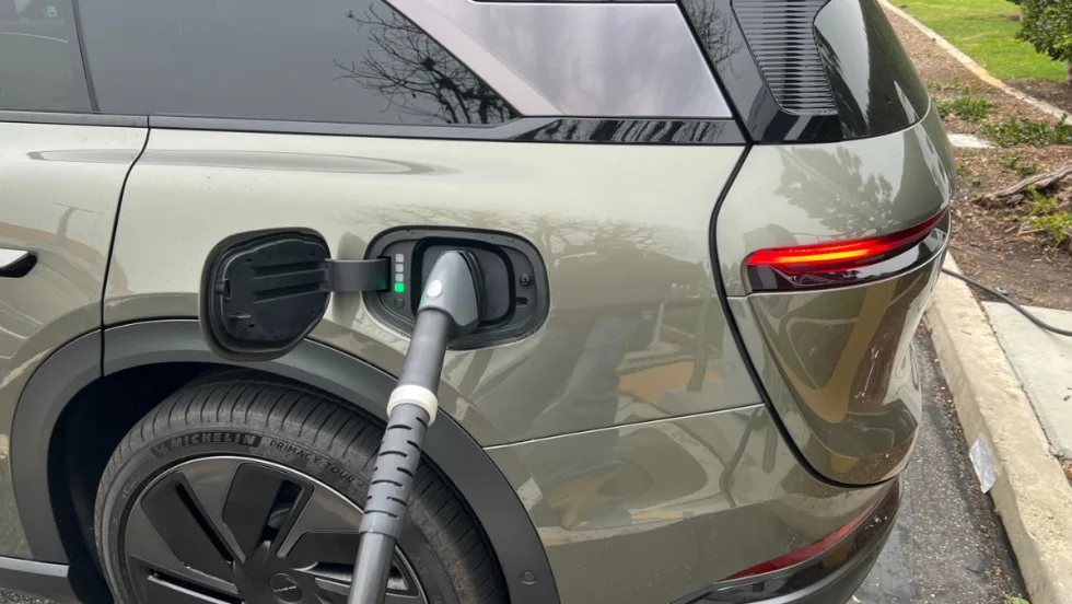 A Lucid Gravity parked at a charging station with a charging cord inserted into the port.