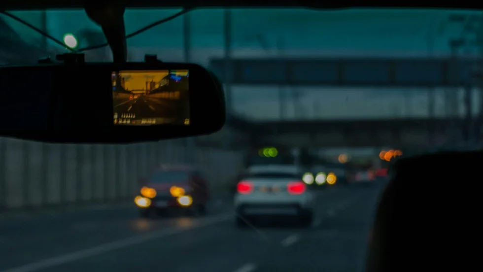 Looking through the windshield of a car from the interior, a dashcam is connected to the rearview mirror.
