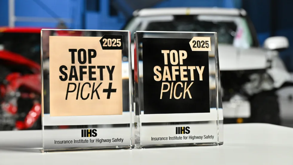 Close up image of Top Safety Pick+ and Top Safety Pick awards in front of crash test cars.