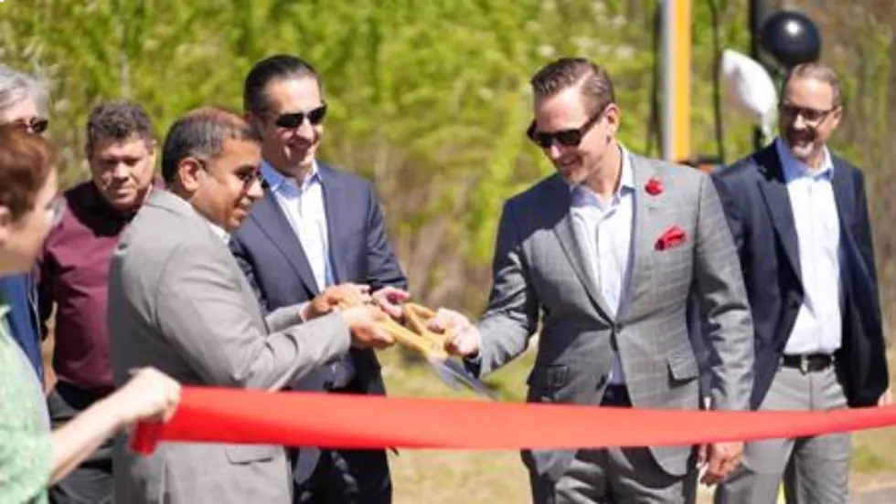 Three men in suits cut a red ribbon at an outdoor opening ceremony.
