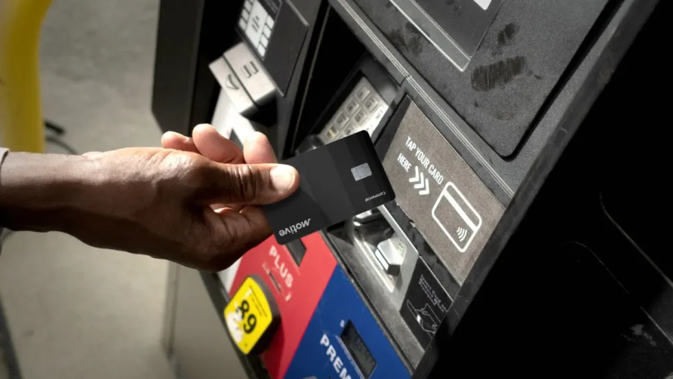 A hand holding the black Motive card for fleets is about to insert the card at a gas pump.