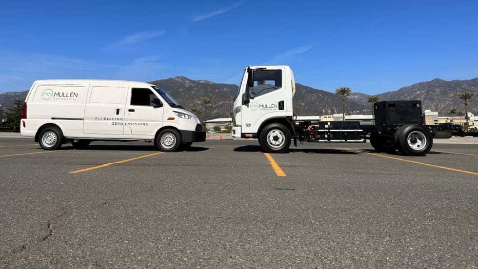 An electric cargo van and a Class 3 cab chassis sit in a parking lot facing each other.
