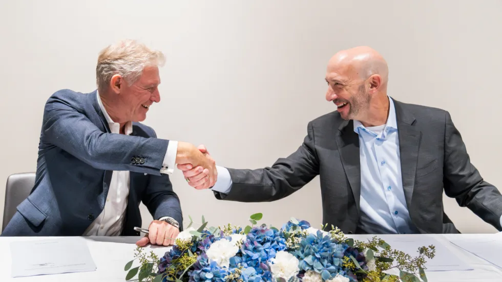 Tim Albertsen and Shlomo Crandus shake hands at a table with a blue flower bouquet on it.