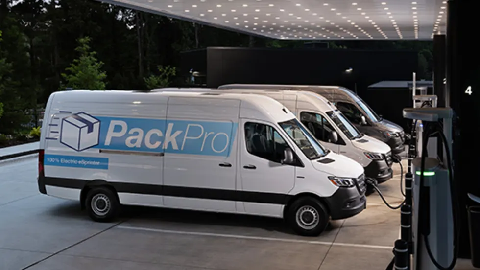 Row of white electric delivery vans labeled ‘PackPro’ charging at a modern outdoor EV station .