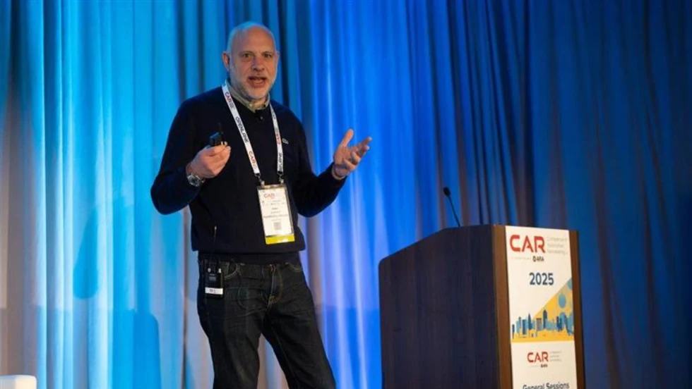 Speaker presenting on stage at the 2025 CAR Conference, standing beside a podium with event branding and sponsor logos.