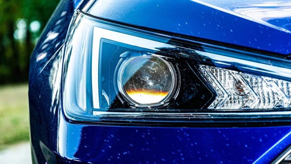Close up of a blue car’s headlight with white marks or scratches on the surrounding auto body.