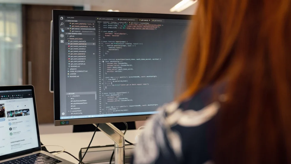 The back of worker positioned in front of two computer screens.