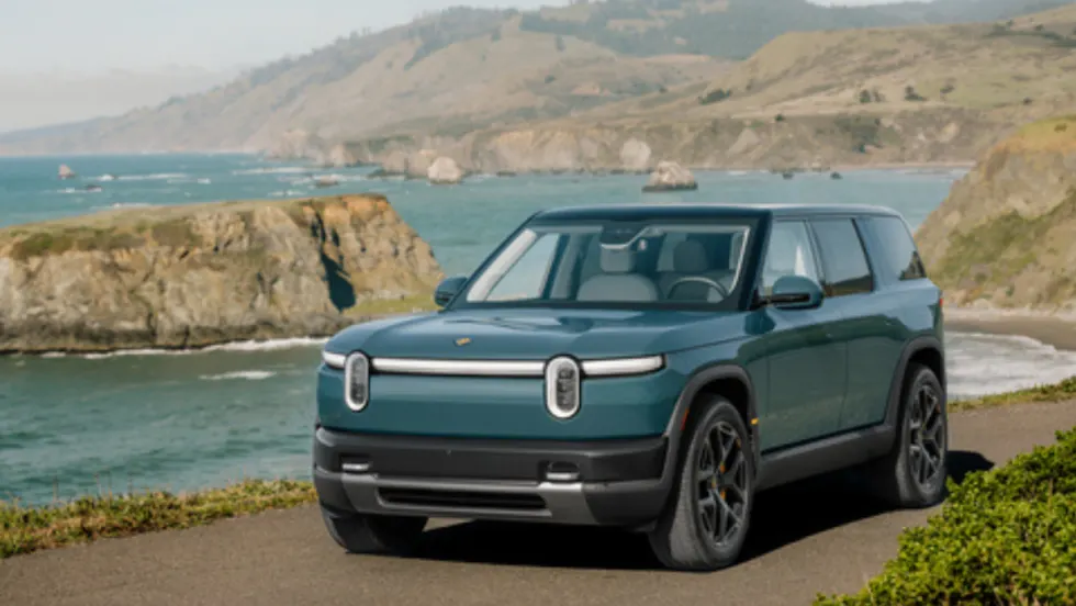 Rivian R2 electric SUV parked along a coastal road with ocean cliffs in the background, showcasing the midsize EV’s design and outdoor capability.