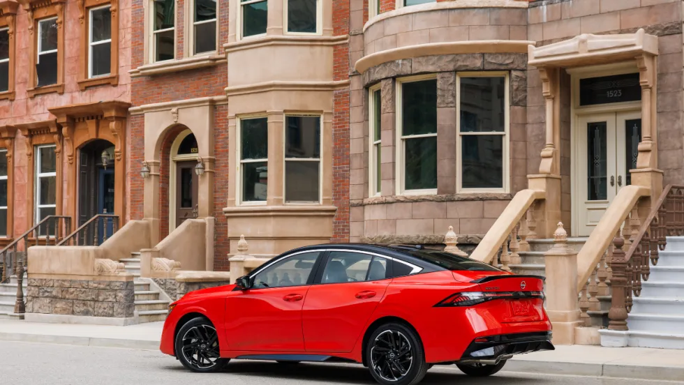 A 2026 red Nissan Sentra sits in front of a row of buildings. 