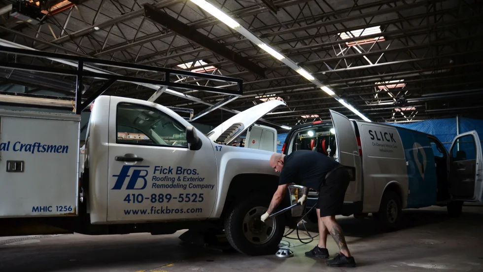 Technician services a commercial van inside a repair facility while a utility truck is parked beside it.