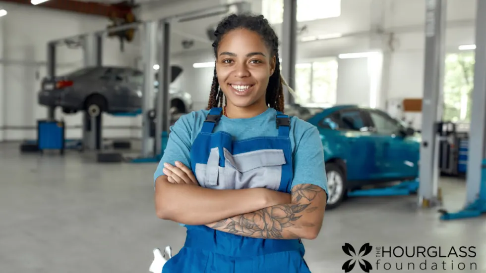 A woman in a blue shirt and apron stands in an automotive suite with her arms crossed. 