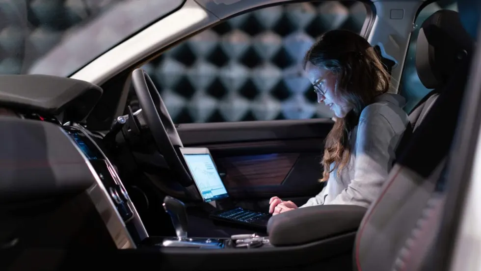 Data analyst looking at computer screen while seated in front of vehicle.