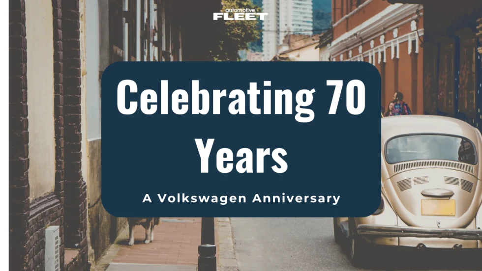 A vintage VW bug drives on a street between buildings.