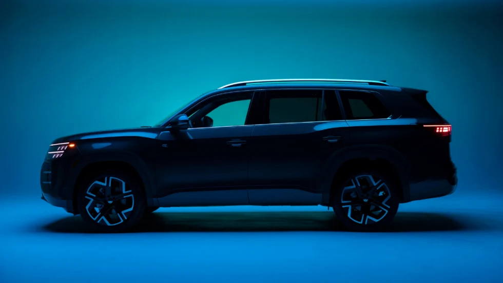Side profile of a dark Volkswagen Atlas SUV in a studio setting with blue lighting, highlighting updated design and exterior styling.