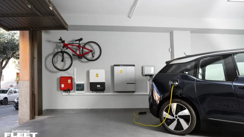 Electric vehicle charging in a home garage with wall-mounted charging and energy systems, illustrating WEX EV At-Home fraud protection and fleet charging verification technology.