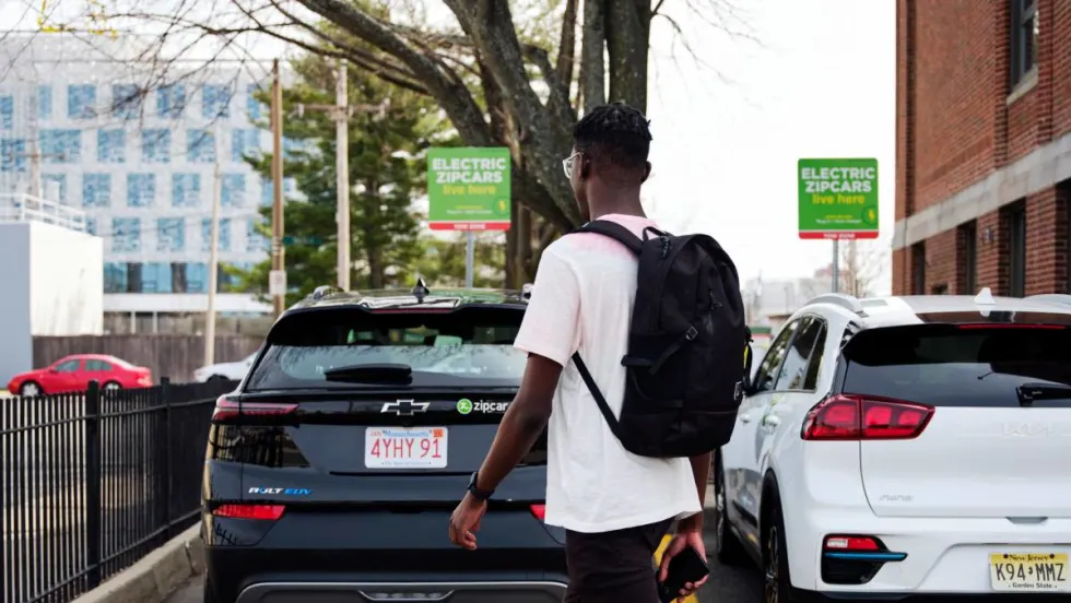 Man with a backpack walking behind carsharing vehicles.