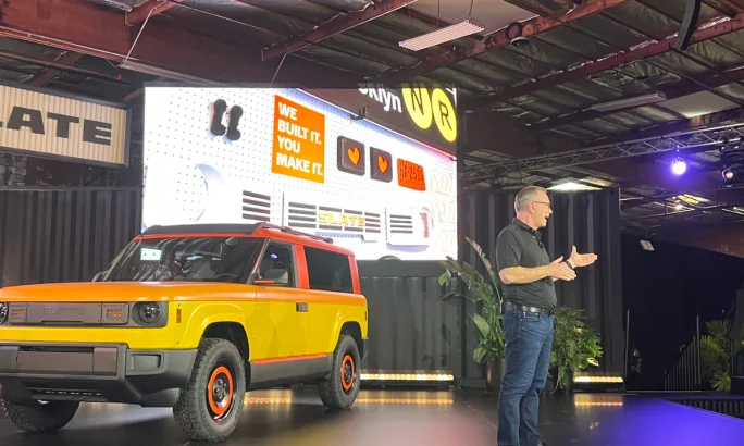 Slate CEO Peter Faricy on stage with a yellow SUV model during the debut event.