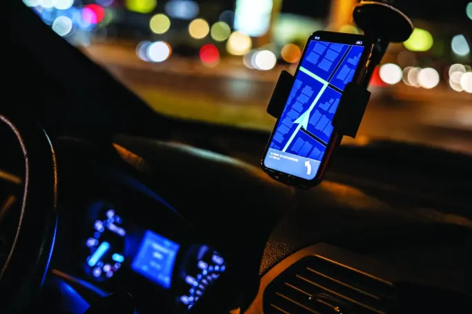  Smartphone mounted on a vehicle dashboard displays turn-by-turn navigation while driving at night.
