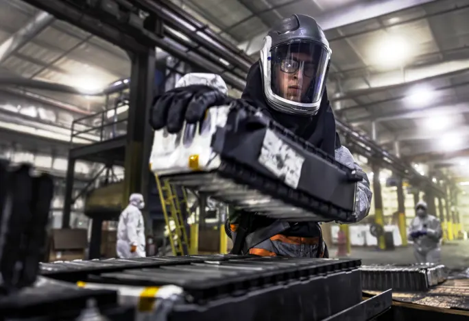 A technician in safety equipment is engaged in recycling work on a battery, ensuring safety and precision.