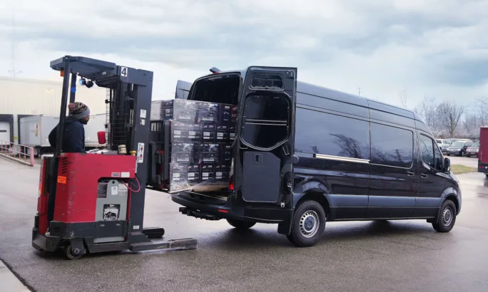 Forklift loading cargo into a Sprinter van through rear door.