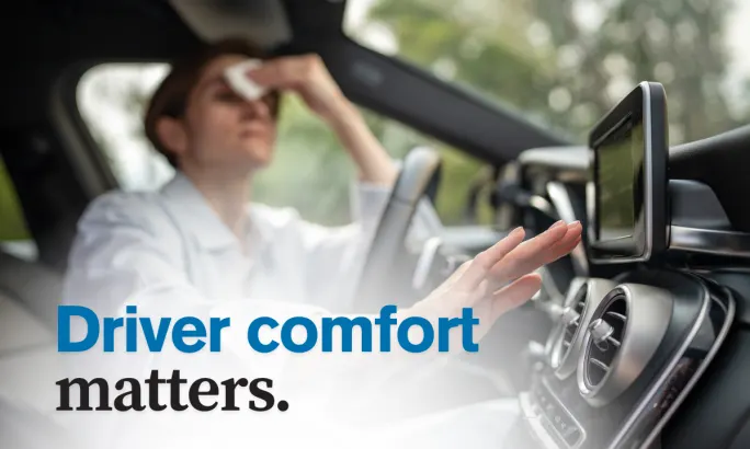 Person wiping sweat from forehead inside a vehicle, reaching for A/C controls, highlighting the importance of keeping drivers cool and comfortable.