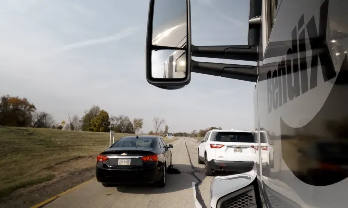 Side mirror view from a Bendix truck showing nearby black and white vehicles on a highway.