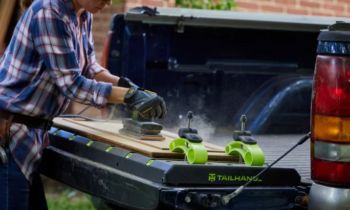 Worker cutting wood on a pickup tailgate.
