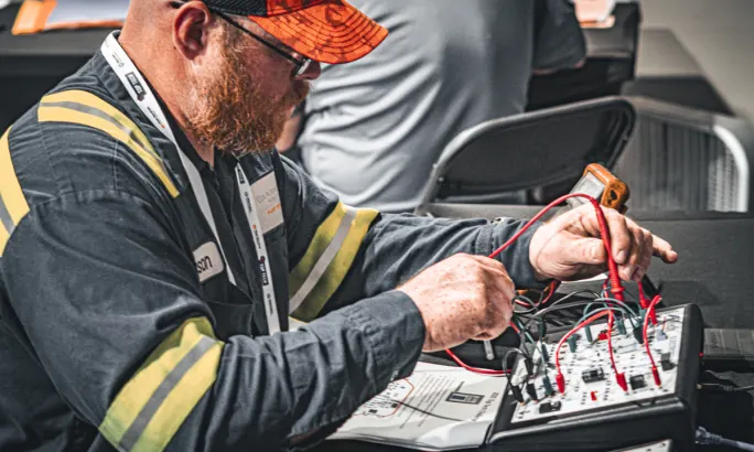 Technician using diagnostic tools to test truck electrical circuits at Top Tech 2025 competition.