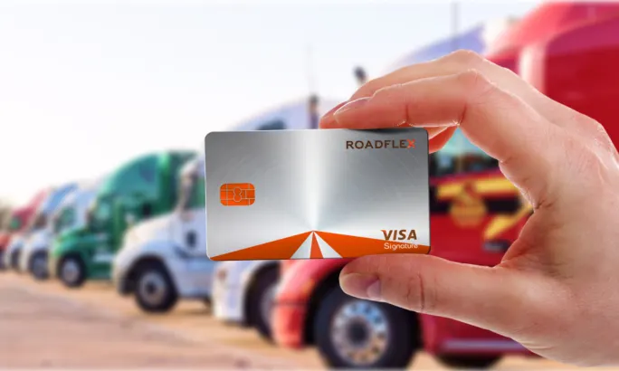 Hand holding a RoadFlex Visa fleet card in front of parked semi-trucks, representing AI-powered fuel and expense management for fleets.