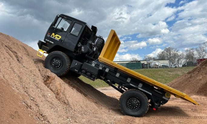 Black Acela truck with yellow dump bed climbing steep dirt incline, showcasing extreme off-road performance.