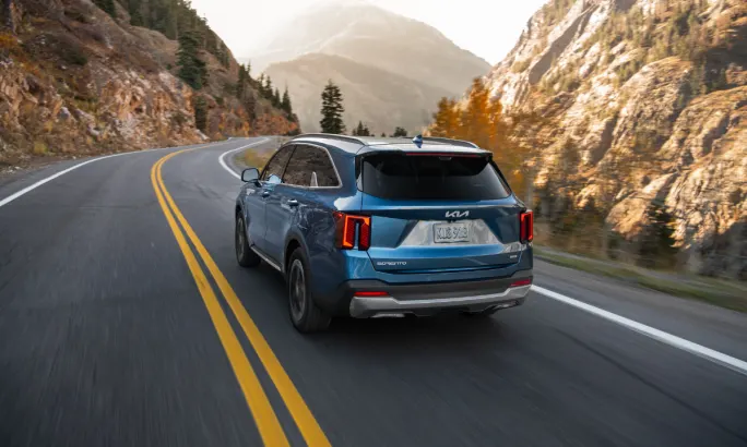 Rear view of a blue 2026 Kia Sorento Hybrid driving on a curved mountain road.