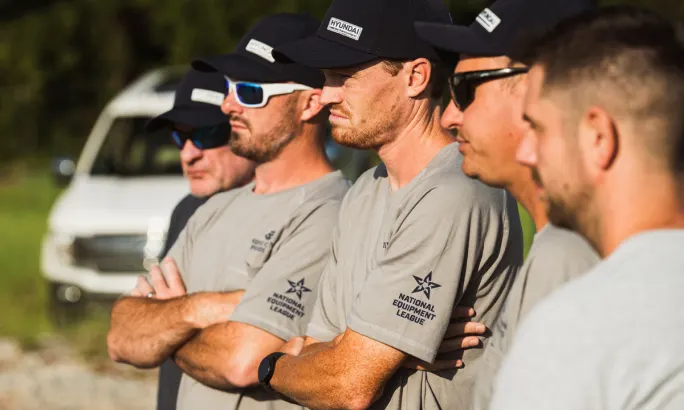 Close-up of competitors in National Equipment League shirts and hats during an event briefing.
