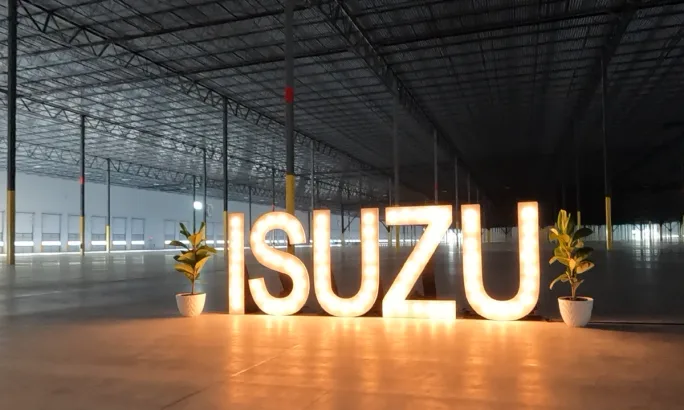 Illuminated Isuzu sign inside a large industrial building that is empty.
