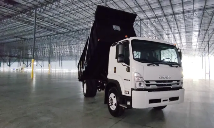 A white Isuzu dump bed truck parked inside a large industrial building.