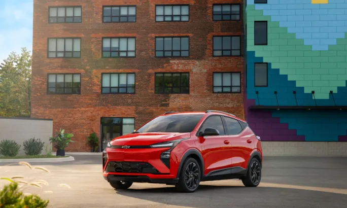 Red 2027 Chevrolet Bolt RS parked in front of a brick building with colorful mural.