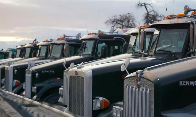 Line of parked Kenworth trucks representing commercial fleets vulnerable to facility damage during earthquakes.