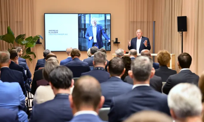Businessman in front of a room of seated business people as he talks to them. 