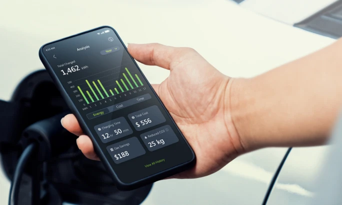 Hand holding a smartphone displaying the MSI aConnect app with EV charging statistics and energy tracking information.