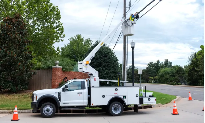 A bucket truck extended and a worker repairing utility lines.