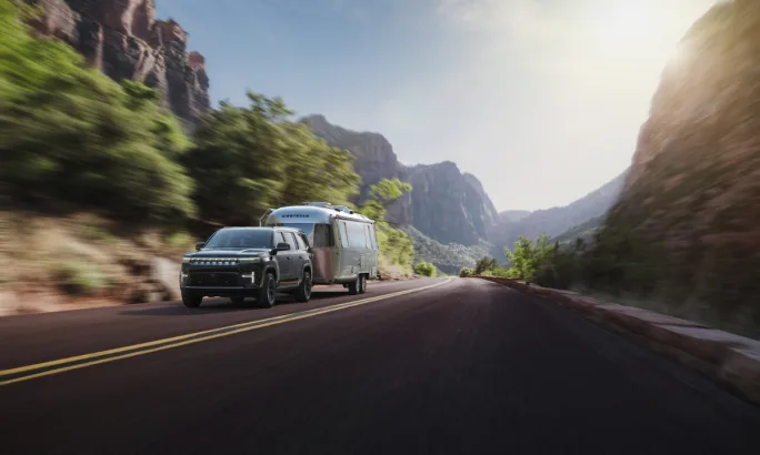2026 Jeep Grand Wagoneer towing an Airstream trailer along a mountain highway.