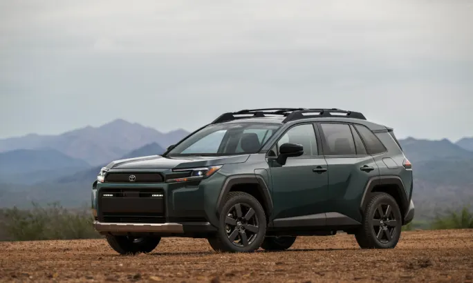 Dark green 2026 Toyota RAV4 Woodland grade SUV parked on a dirt trail with mountains in the background.
